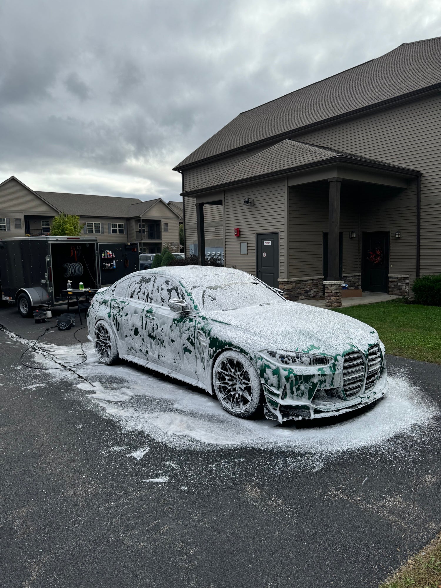 Car covered in soap suds parked on a driveway with a house in the background