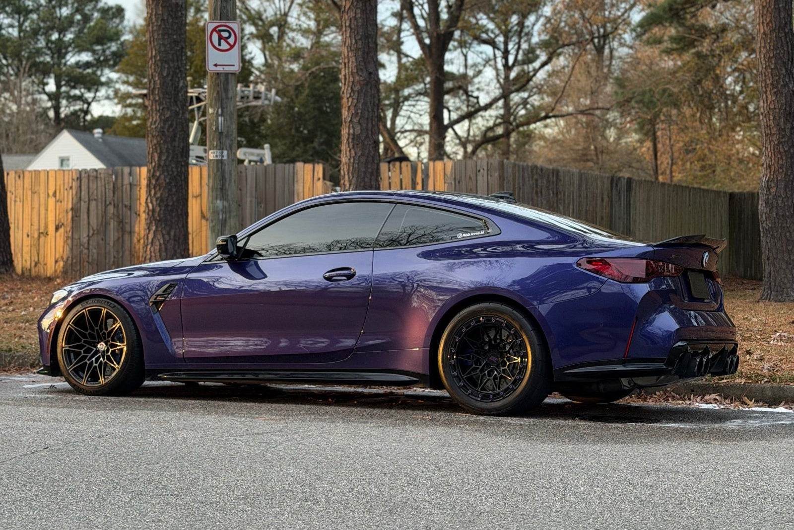 Blue sports car parked on a street with trees and a fence in the background